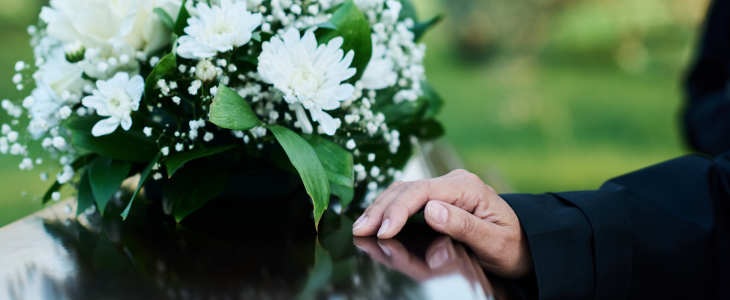 Hand resting on a casket with a flower arrangement on top in North Dakota, related to personal injury attorney