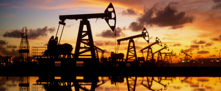 Pump jack silhouette against a sunset sky with reflections in the water.