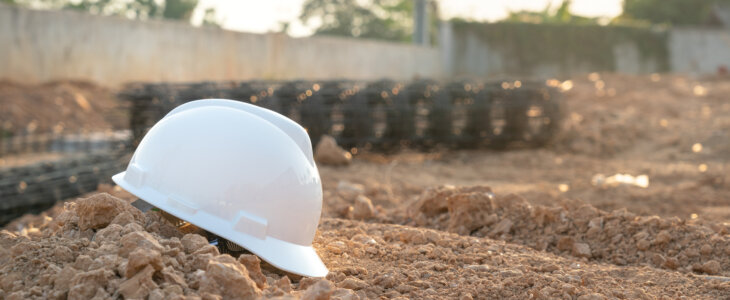 A white safety hardhat helmet is placed on dirt ground at the construction work site, unsafe workplace. Safety PPE object photo.